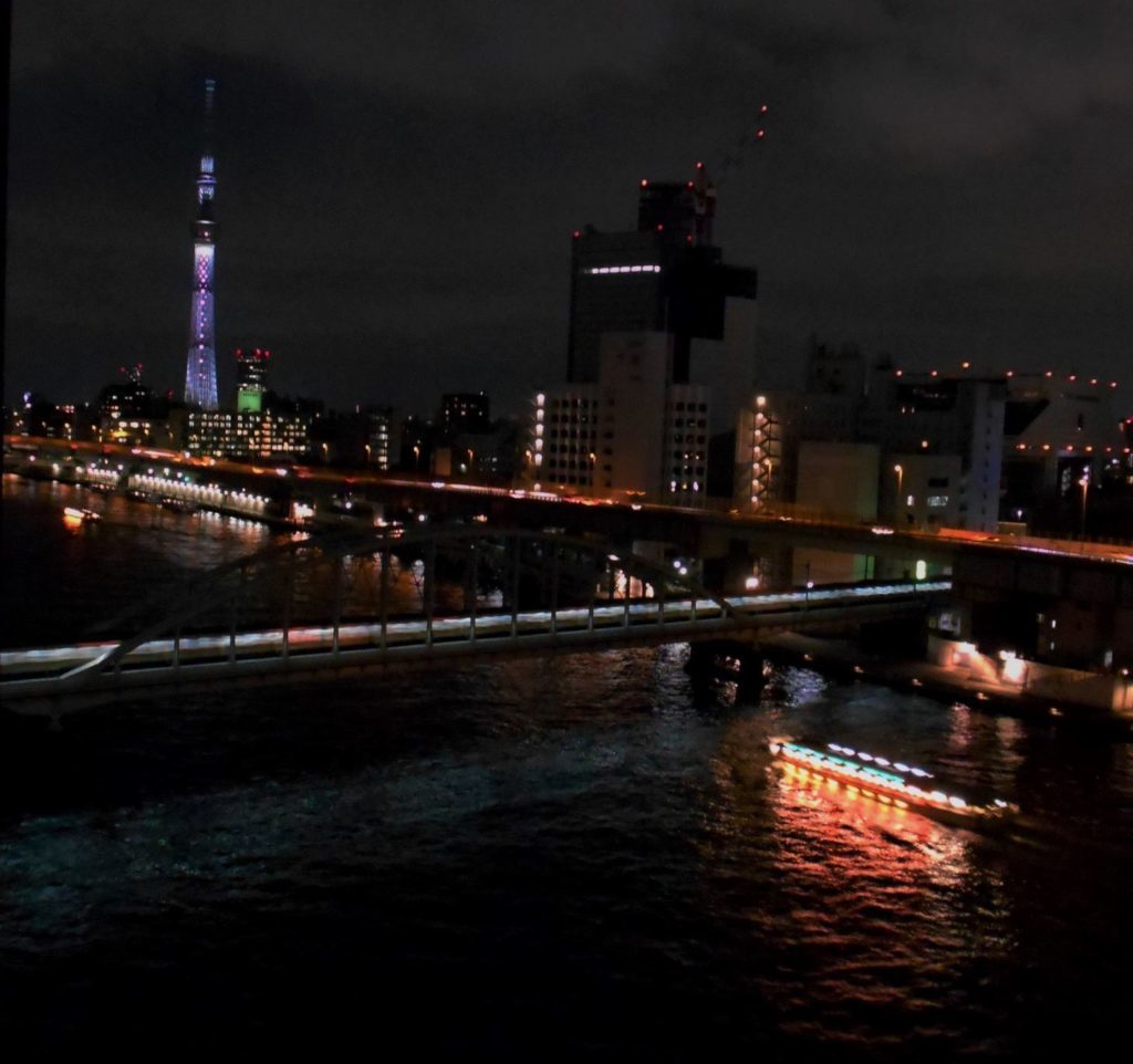 夜の隅田川橋梁に、電車と屋形舟、スカイツリーがライトアップして共演している画像。